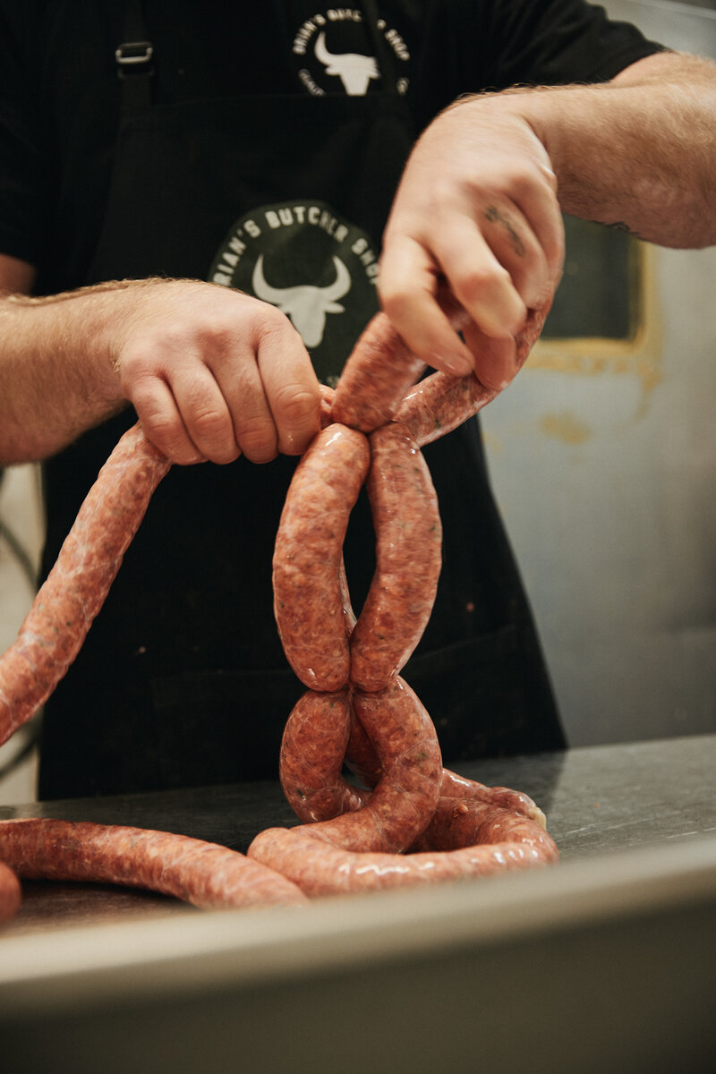 Hands linking fresh sausages at Brian’s Butcher